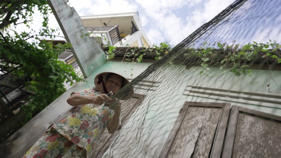 Góc thấp, bà cụ vá lưới dưới mái hiên